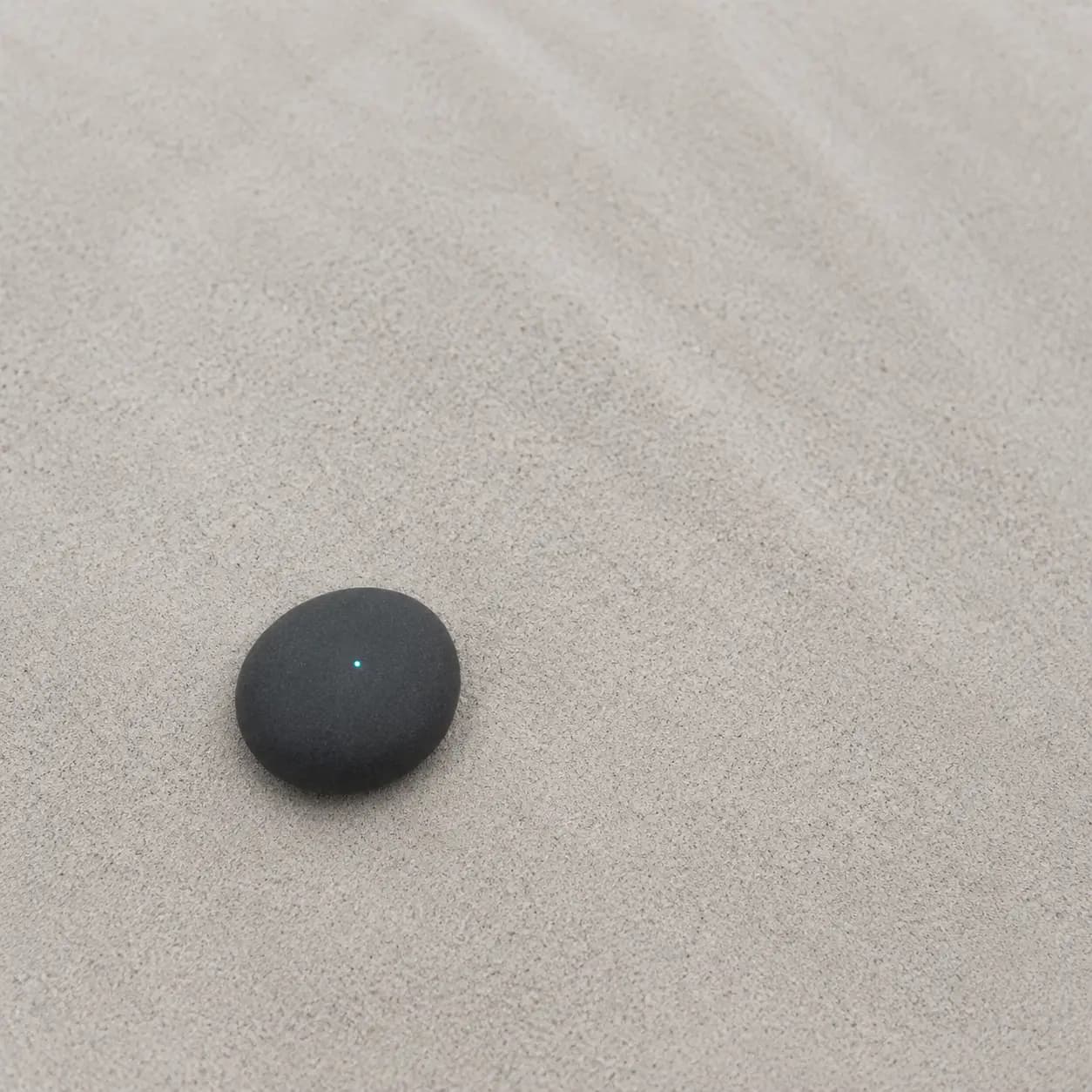 A smooth graphite stone with one small teal signal on pale sand