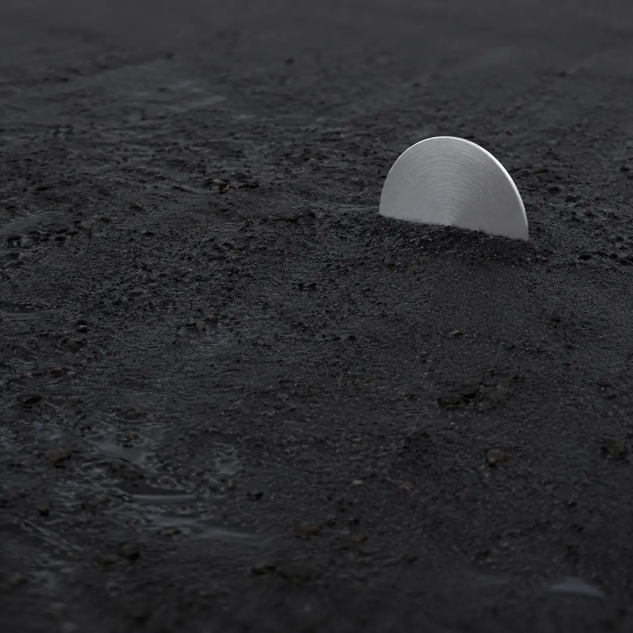 A brushed aluminium disc emerging from dark wet coastal sand